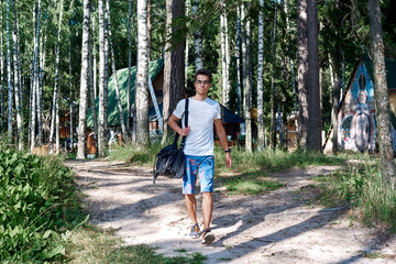 Young man walking on forest trailway near cosy forest houses, Weekend activities in summer