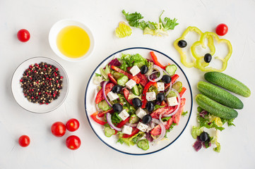 Greek salad of Vegetable and feta cheese on a white concrete background and the ingredients from which it is made.