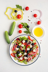 Greek vegetable salad with feta cheese and ingredients from which it is cooked on a white concrete background. Vertical photo.