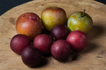 Plums on a black background. Plums of two varieties lie on a wooden surface. Summer harvest