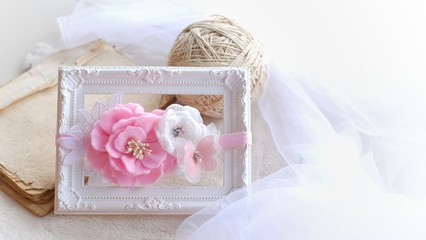 Fototapeta na wymiar Handmade flower as headband hair accessory made out of fabric flowers in beautiful pastel pink color on a beautiful and vintage white photo frame