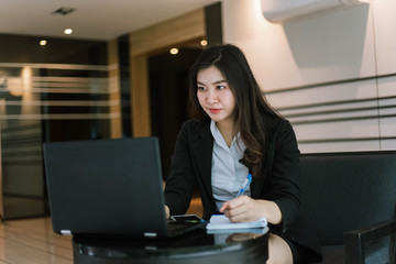 Beautiful young asian woman in suit using laptop and writing note
