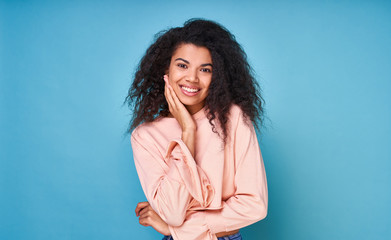 Fototapeta premium A cute gentle young African-American woman poses against a blue background.