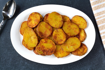 Fried spicy potato slices on a white plate