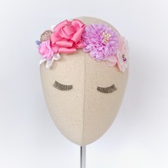 A head mannequin wearing handmade flower headband hair accessory made out of fabric flowers in beautiful pastel colors