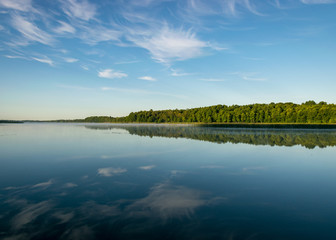 Fototapeta na wymiar cloud reflections in clear and calm lake water, forest in the background, summer morning