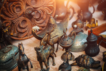 Vintage metal trinkets of deer, horse, tiger and turtle next to  metal oil lamp, scale of justice, jugs and box on the countertop at sunday flea market. Vintage furniture  in antique bazaar.