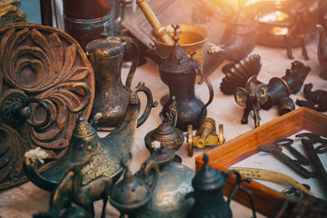 Vintage metal trinkets of elephant, cannon, deer next to metal oil lamp, rusty keys and bronze mortar,  jugs and on the countertop at sunday flea market. Vintage furniture in antique bazaar.