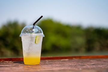 A Plastic glass of honey lemon soda put on wooden table with background of sky and tree