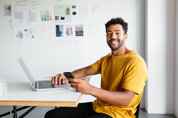 Cheerful male event planner with smartphone and laptop