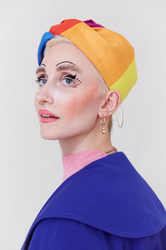 A stylish woman wearing a beautiful rainbow hat and a unique makeup look.