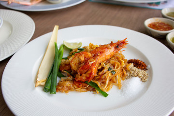 Fried noodles Pad Thai with prawn, piece of banana blossom and chive on white plate