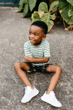 An adorable, stylish little boy sitting outside on the concrete.
