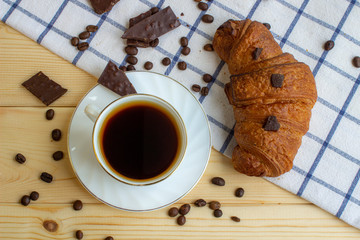 Coffee and a croissant on a wooden background. Visa from above