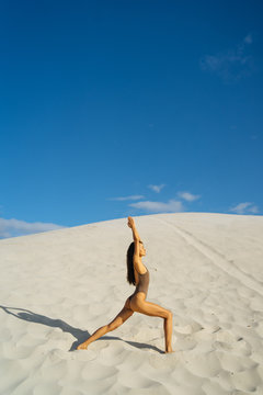 Slender woman practicing warrior pose on desert background