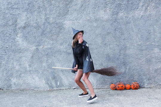 A blond woman in a witch's costume is holding a broom and having fun outdoor