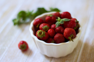 Ripe red strawberries in a white bowl on a light wooden background. Delicious and healthy food. Healthy organic products concept. Harvesting.