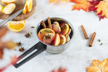 Hot mulled wine with citrus, apples, cinnamon sticks, and anise in cooking pan on grey table...