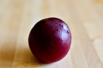 A plum on a wooden table covered with dew after being in the refrigerator.