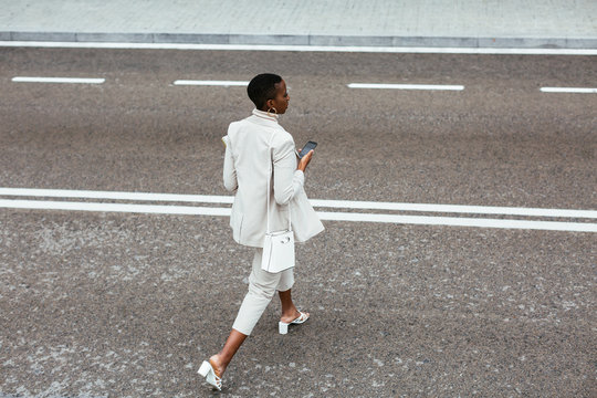 Black boss with smartphone crossing road