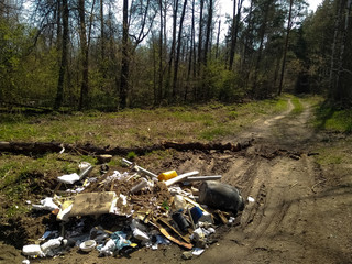 A huge mountain of household waste lies on the road in a green, blooming forest.