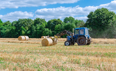 straw in round bales and a tractor in the field