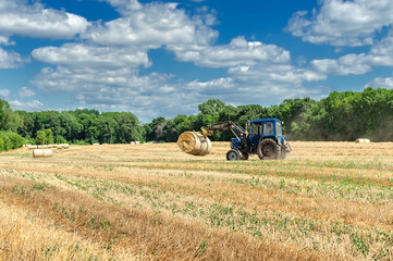 straw in round bales and a tractor in the field