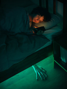 Helloween story. The girl uses a smartphone in bed, and a mystical light shines under the bed.
