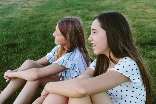 Two young girls sitting on the grass smiling looking to the left