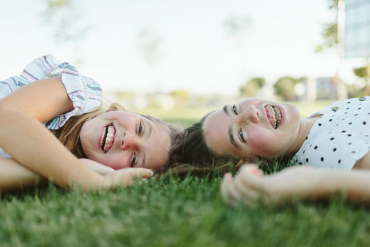 Two teenage girls lying on the grass laughing looking at camera.