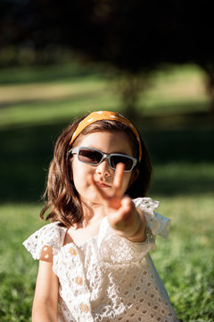 cute little girl looking at camera while wearing sunglasses at sunset at a park
