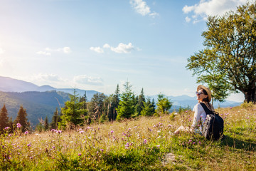 Naklejka na ściany i meble Traveling in summer Ukraine. Trip to Carpathian mountains. Happy woman tourist hiking sitting in flowers