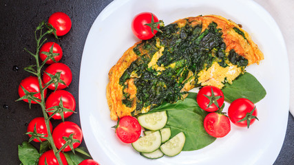 fried eggs with spinach and tomatoes, cucumbers on a white large plate on a black embossed table. top view, copy space
