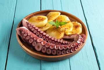 Cooked octopus dish served with sliced boiled potatoes, smoked paprika and olive oil. on blue wooden background