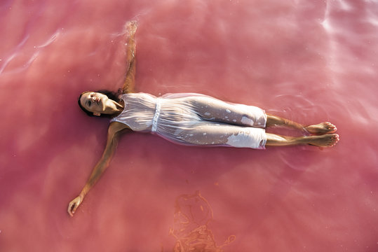 Aerial view of a beautiful sweet woman lying floating on pink lake