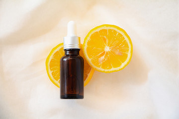 Bottle of lemon essential oil with lemons slice on white fabric background. Top view flat lay. Beauty cosmetic natural skincare product mock up.