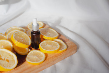 Bottle of lemon essential oil on a wooden with lemons on white fabric background. Beauty cosmetic natural skincare product mock up.
