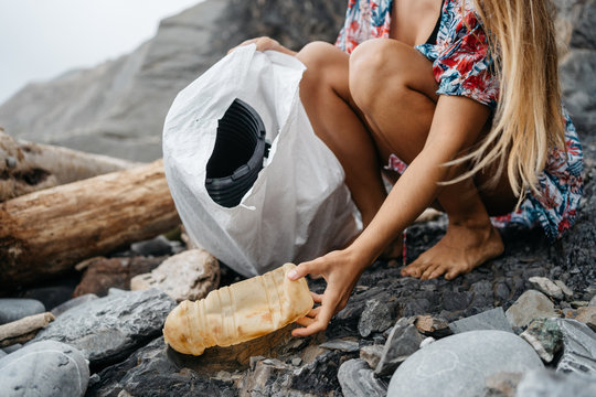 Anonymous young girl picking up plastic waste from beach