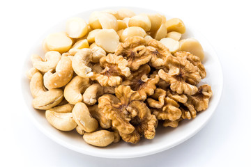Variety of fresh nuts on a white dish above the white background