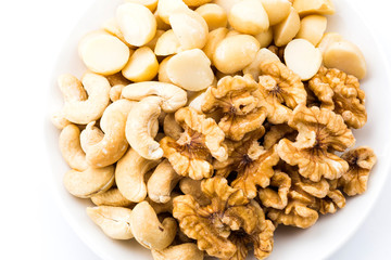 Variety of fresh nuts on a white dish above the white background