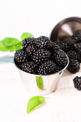 Ripe blackberries with basil leaves in a metal bowl on a wooden table