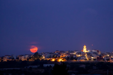 full moon rising over the horizon of a town