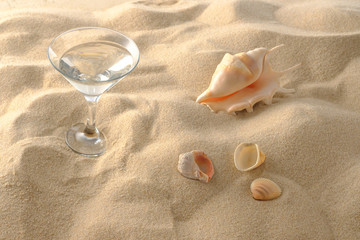 Fototapeta na wymiar Beach vacation concept. Cool drinks on the beach sand. A glass of refreshing drink and seashell. Close-up.