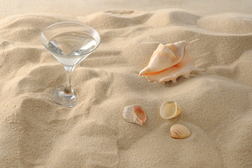 Beach vacation concept. Cool drinks on the beach sand. A glass of refreshing drink and seashell. Close-up.