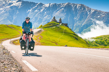 Cyclist on the road in scenic caucasus nature with Gergeti trinity monastery in the background....