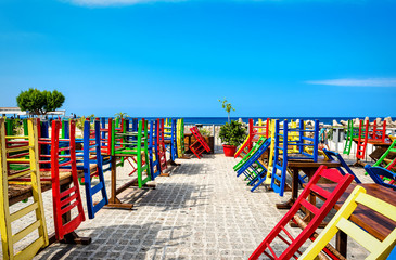 Many upside down different colour chaires placed on the tabes, with blue sea and sky at the background