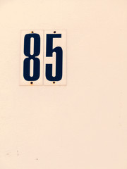 Metal plate with figures 85 on concrete wall painted with light paint, house number. Suitable as background for any your project.