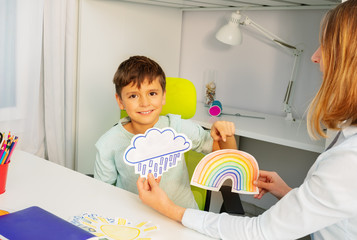 Little boy during aba development therapy sitting selecting between two cards of rainbow and storm