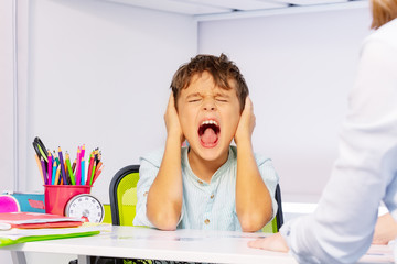 Boy with autism disorder scream and close ears in pain during ABA development therapy sitting by...