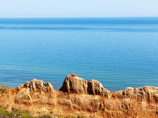 Deep sandy cliff on the background of blue sky. The destruction of the coast as a consequence of soil erosion. Landslide - threat to life.